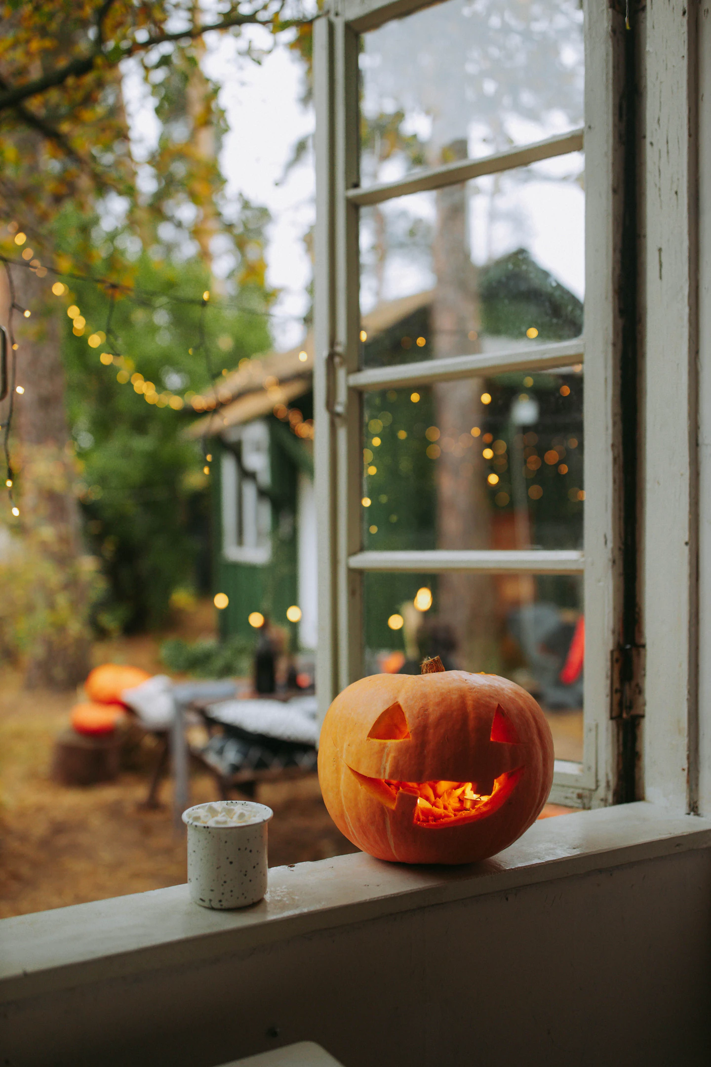 Abóbora de Halloween iluminada junto a uma janela, com luzes desfocadas no exterior.